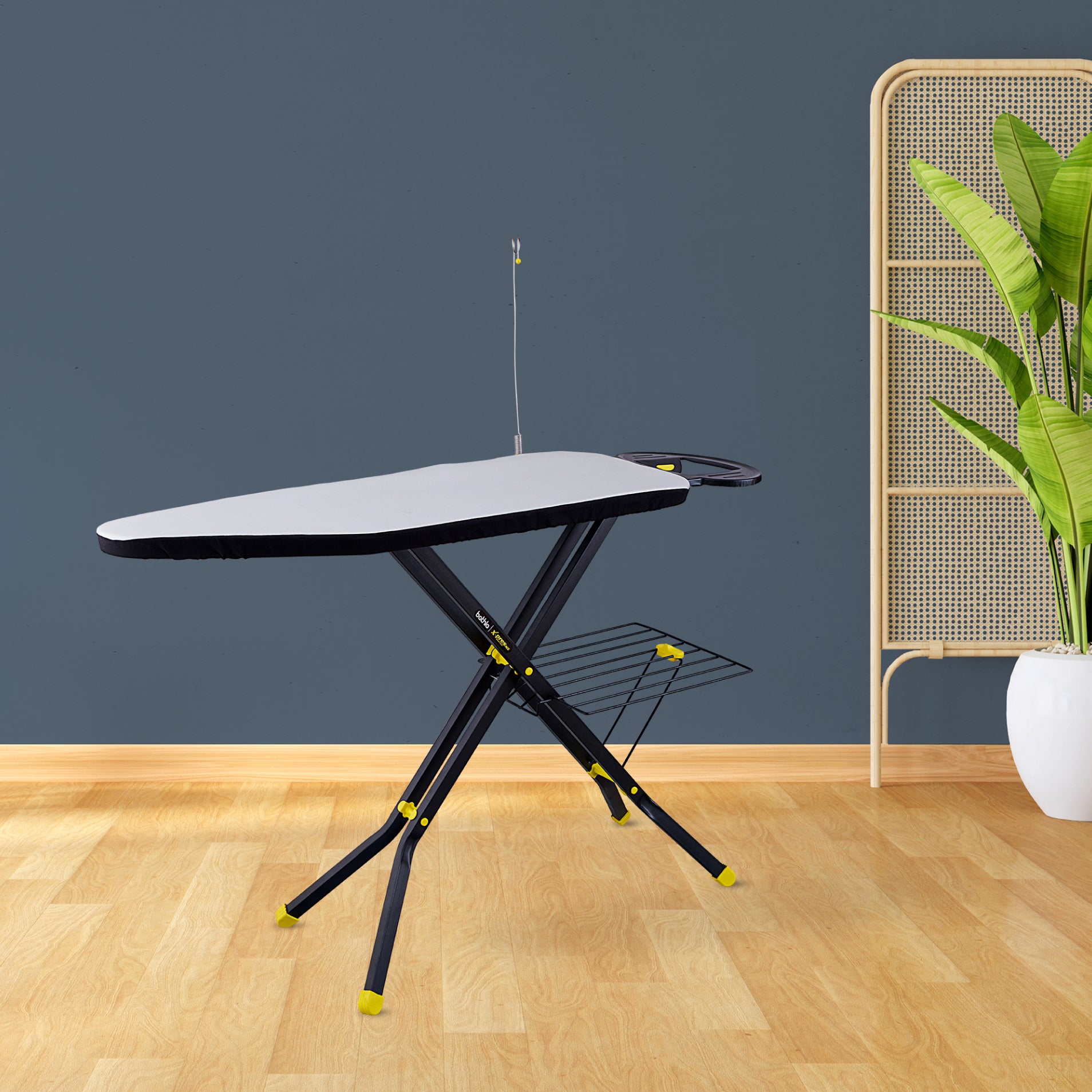 Ironing board with adjustable legs on a wooden floor against a dark blue wall.